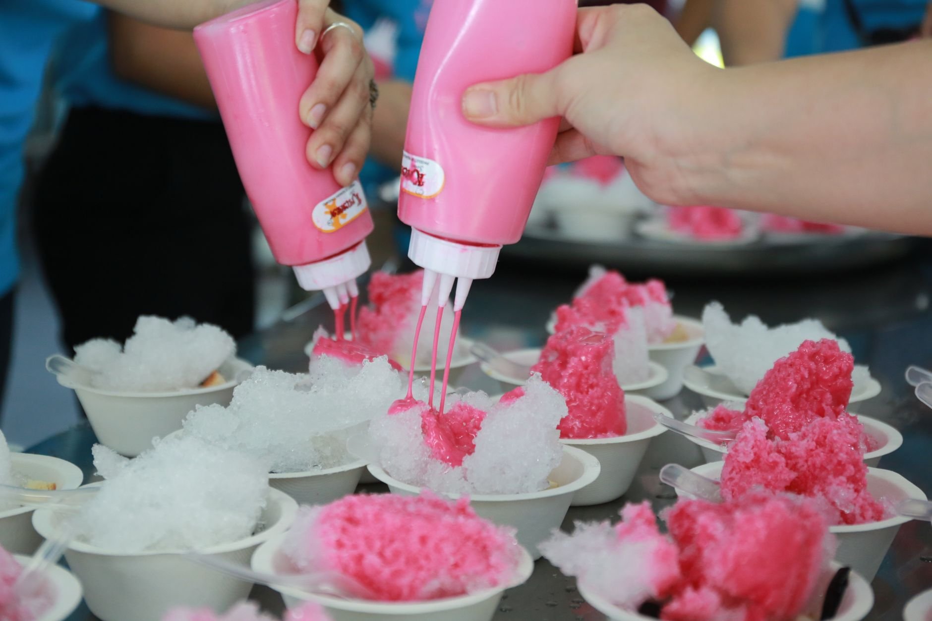 Hands adding syrup to shaved ice desserts creating vibrant treats.