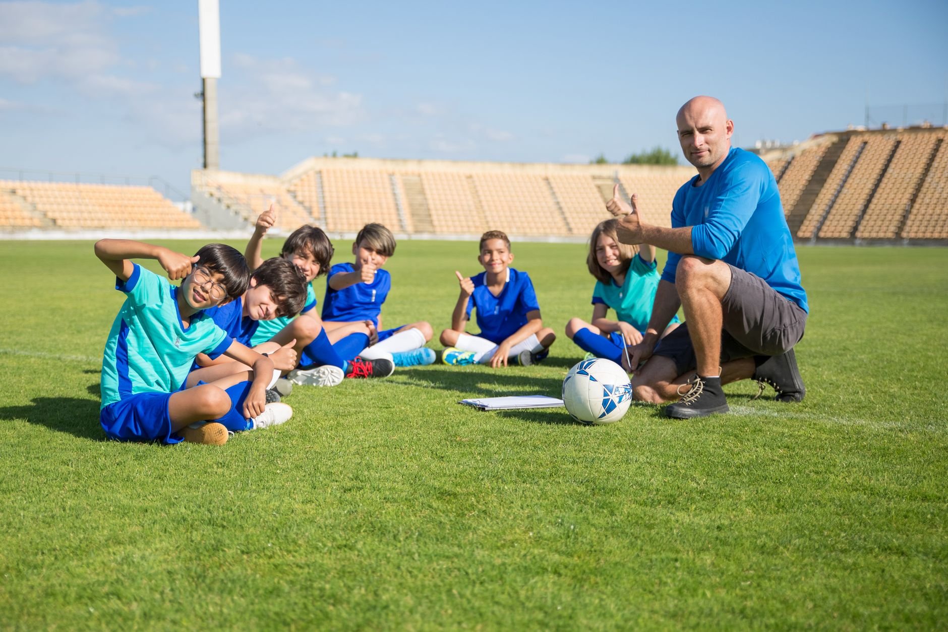 Children enjoying soccer training with coach at an outdoor stadium.